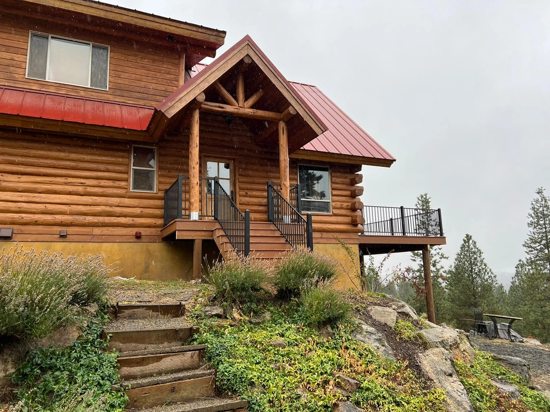Brown deck on a cabin in the woods with a cover and black railing.