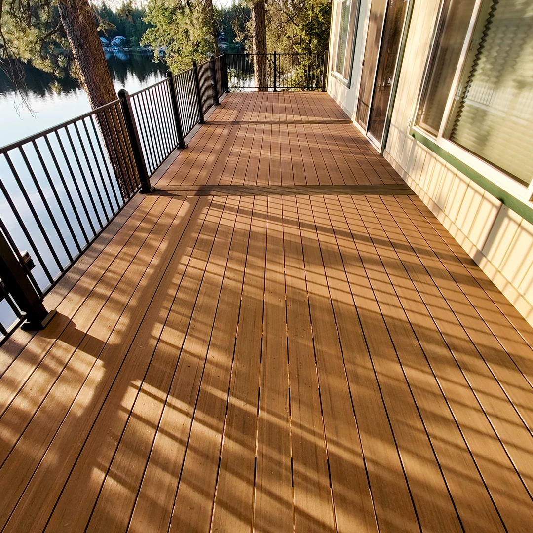 Brown deck in the woods with black railing.