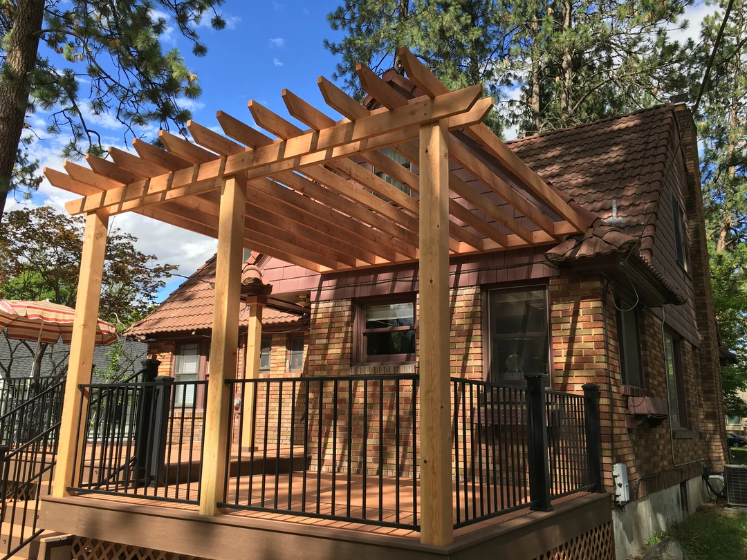 Brown deck with wood pergola and black railing.