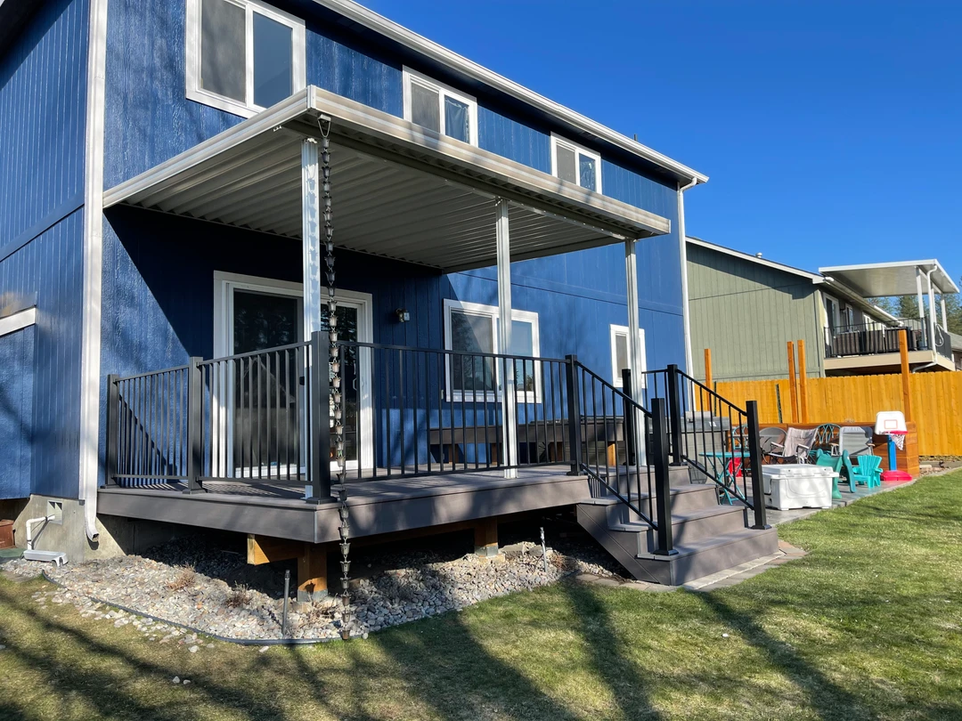 Blue house with deck and black railing. Metal shed style cover is over the deck.