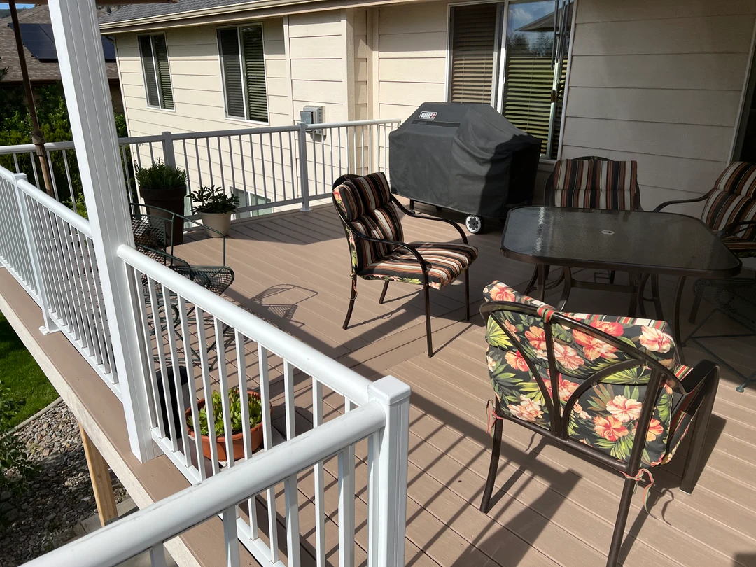 Brown deck with white railing and furniture on it.
